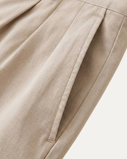 Detailed view of double pleat front design on beige chino shorts fabric