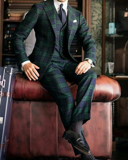 Full length seated view of green and blue tartan formal three piece suit