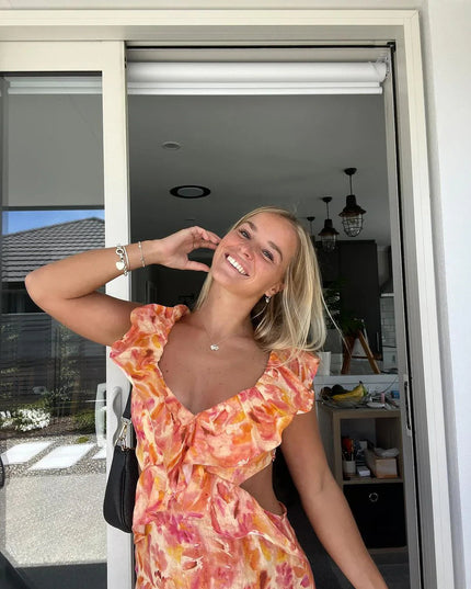 Close-up of a women's floral ruffle tie-back maxi dress in vibrant orange and pink, showing the V-neck and ruffled sleeves.