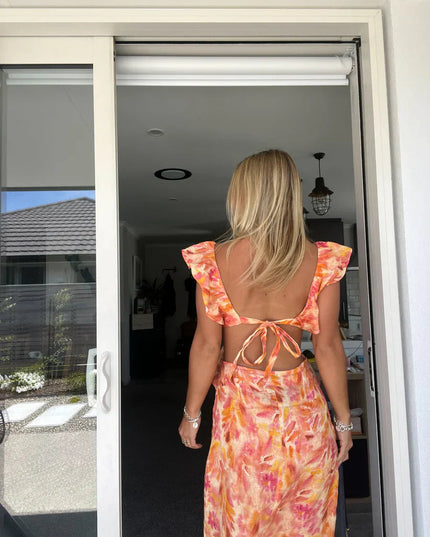 Back view of a women's floral ruffle tie-back maxi sundress, showcasing the open back with a tied bow detail.