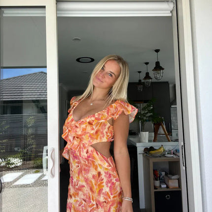 Women's orange and pink floral maxi sundress with ruffle trim and side cutouts, featuring a deep V-neckline.