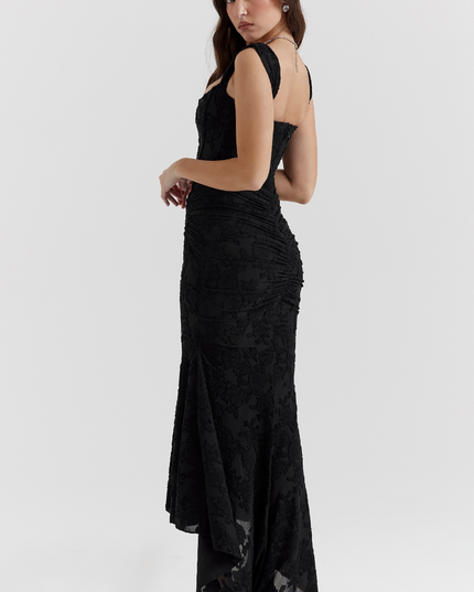 Side view of the black floral corset midi dress, highlighting the fitted silhouette and the dramatic asymmetric skirt with black heels.
