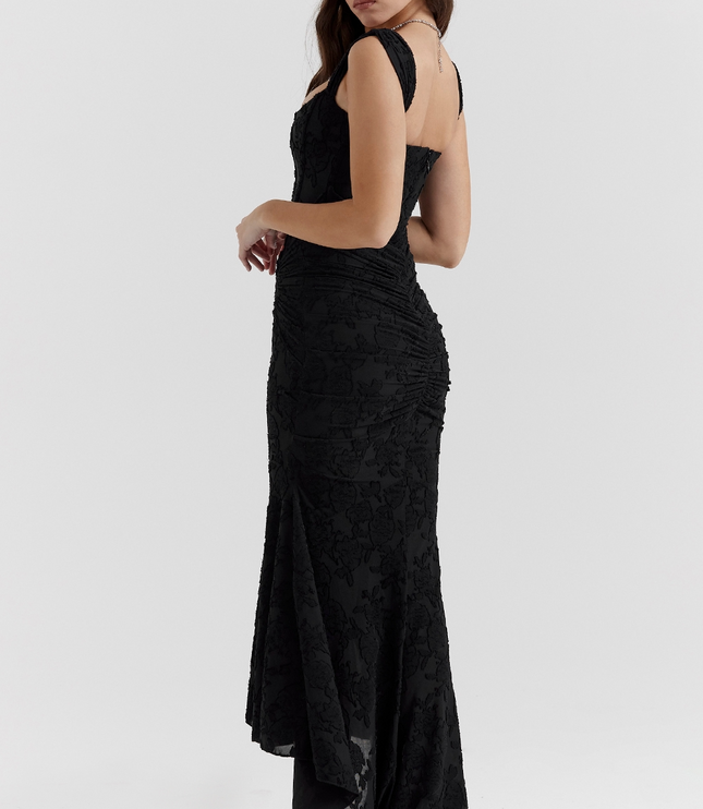 Side view of the black floral corset midi dress, highlighting the fitted silhouette and the dramatic asymmetric skirt with black heels.