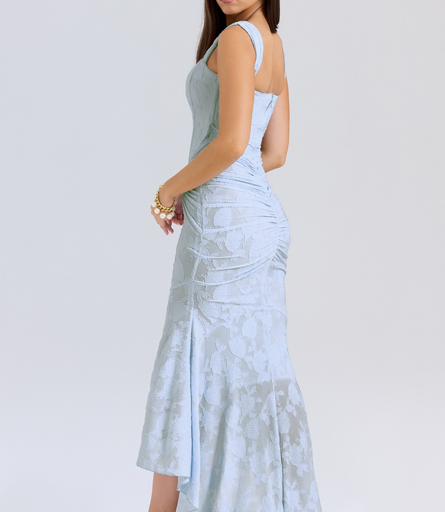 Side view of a light blue women's floral graduation dress, showcasing the fitted corset and draped asymmetric skirt with white heels.