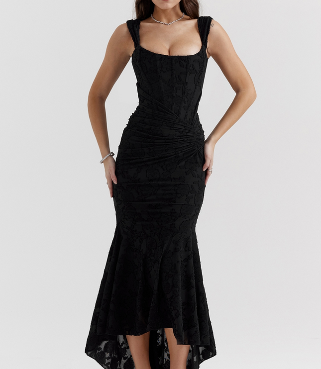 Black women's graduation dress with a subtle floral jacquard design, structured corset, and asymmetric midi skirt, paired with black heels.