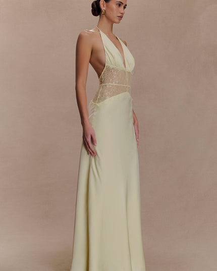 Side profile of a women's light yellow halter neck maxi dress with a deep V-neck and lace inserts.