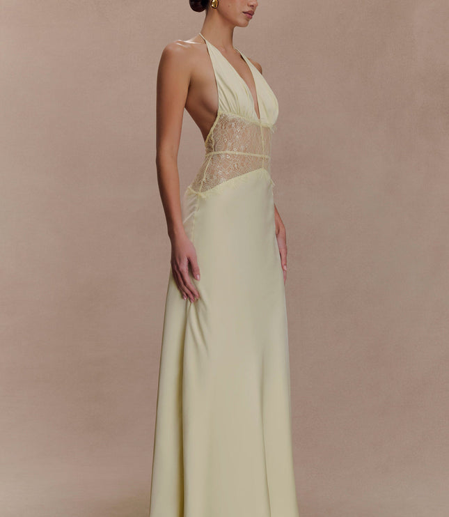 Side profile of a women's light yellow halter neck maxi dress with a deep V-neck and lace inserts.