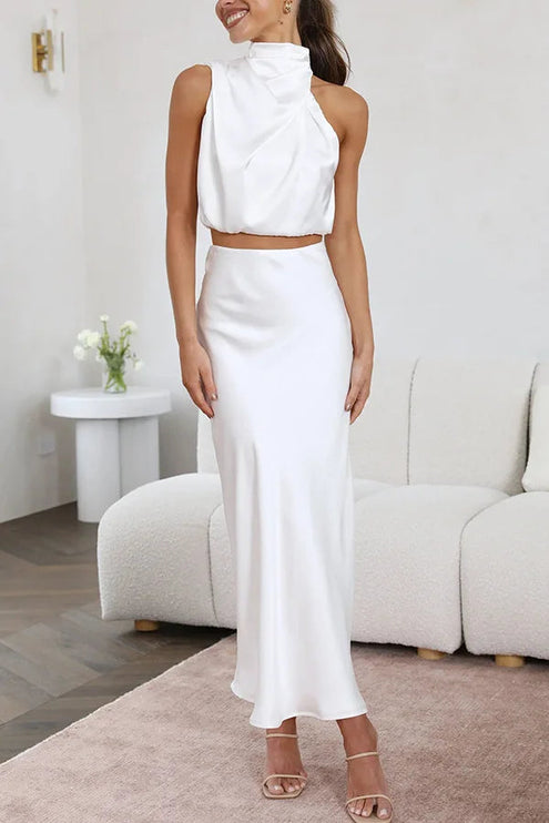 Women's crisp white halter neck satin crop top and elegant maxi skirt set, posing in a bright, minimalist room.
