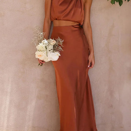 Women's rust orange halter neck satin crop top and matching maxi skirt set, holding a white floral bouquet.