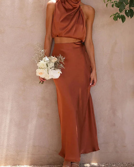 Women's rust orange halter neck satin crop top and matching maxi skirt set, holding a white floral bouquet.