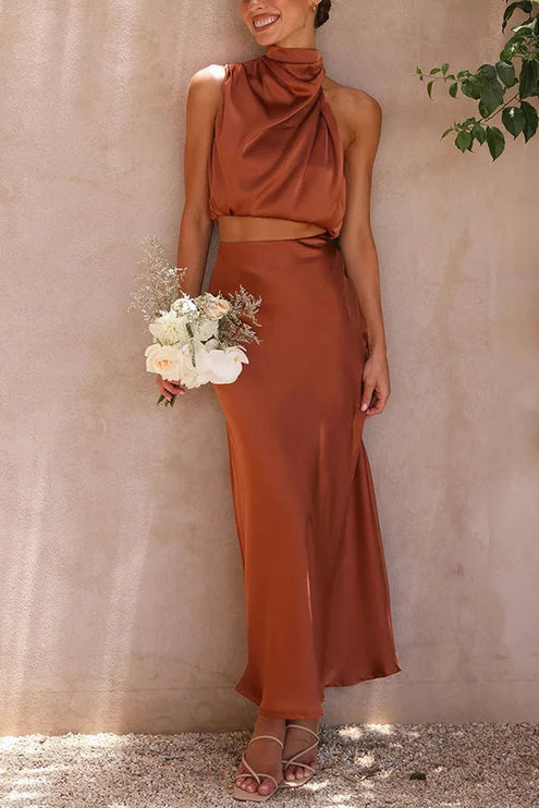 Women's rust orange halter neck satin crop top and matching maxi skirt set, holding a white floral bouquet.