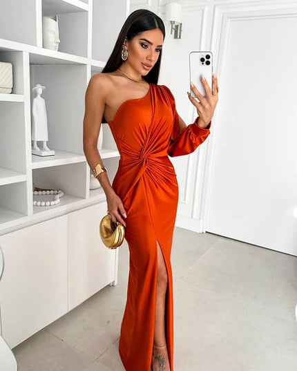 Burnt orange one-shoulder ruched maxi dress with a high slit, worn with a golden clutch and designer shoes.