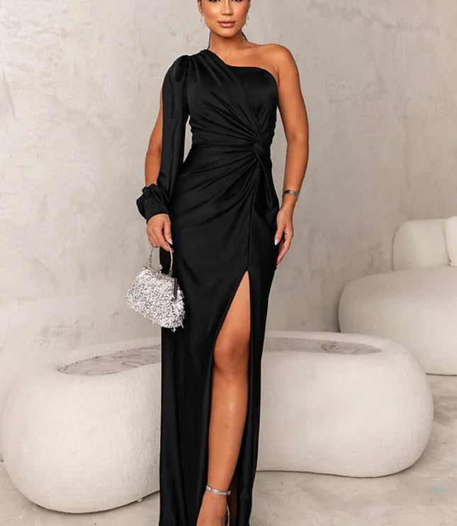 Full length view of a black one shoulder ruched slit maxi dress with silver heels and a matching clutch.