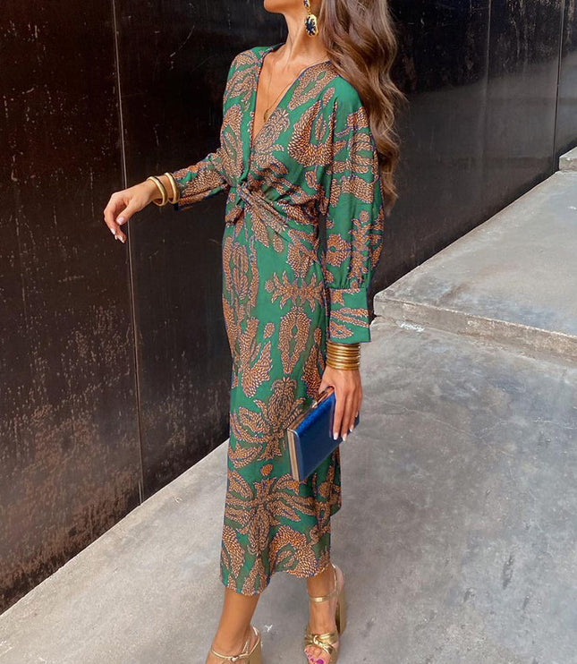 Women's summer midi dress in emerald green with an orange abstract print, V-neck, and long sleeves, styled with gold heels and a blue clutch.