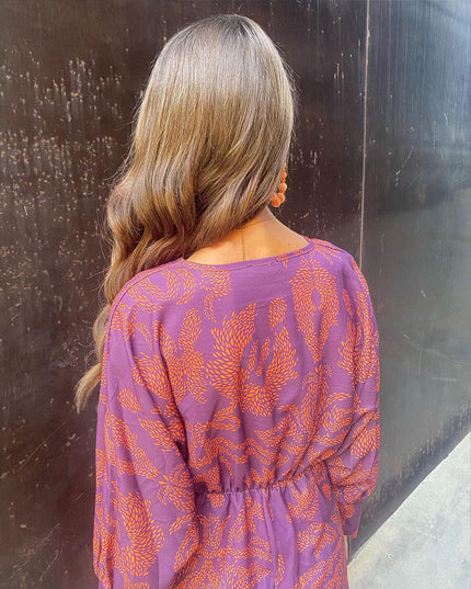 Back view of a women's purple summer midi dress with an orange abstract print and elasticated waist detail.