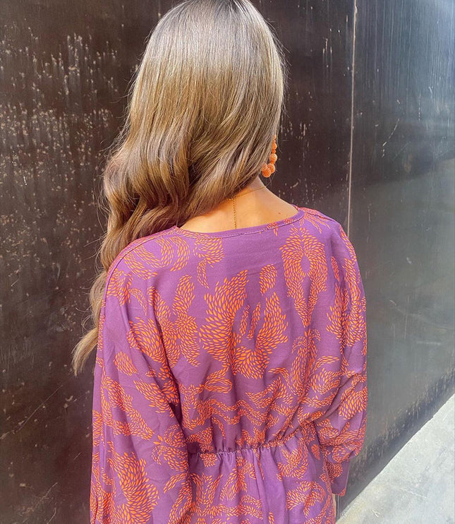 Back view of a women's purple summer midi dress with an orange abstract print and elasticated waist detail.