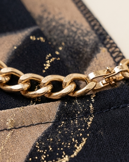 Close-up of abstract print maxi dress fabric showing black and beige pattern with gold chain belt