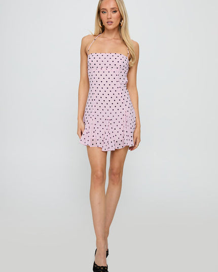 Full view of a pale pink polka dot halter mini dress with black dots, paired with black heels.