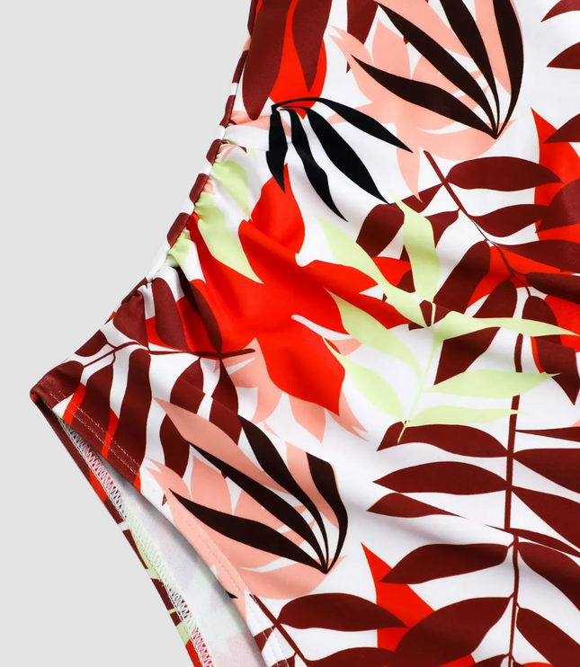 Close-up detail of red leaf print fabric and ruched side seams on swimsuit