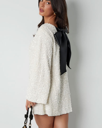 Side view of a white long sleeve mini dress with textured fabric and a large black bow back