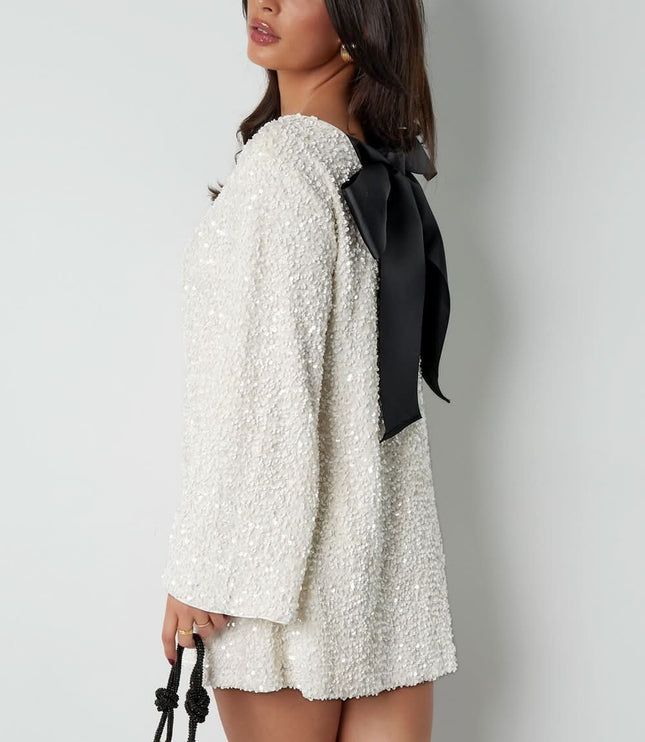 Side view of a white long sleeve mini dress with textured fabric and a large black bow back