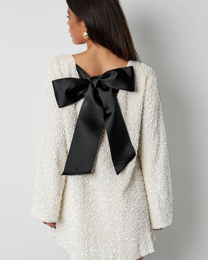 Back view of a white cocktail mini dress with a deep bow back detail and long sleeves