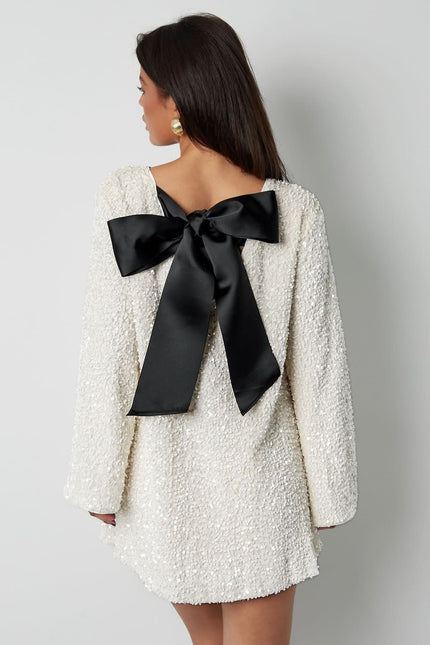 Back view of a white cocktail mini dress with a deep bow back detail and long sleeves
