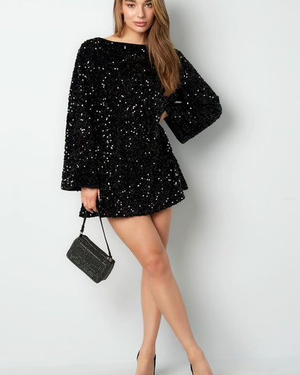 Black sequin mini dress with long bell sleeves and a fitted cocktail silhouette, styled with a small handbag