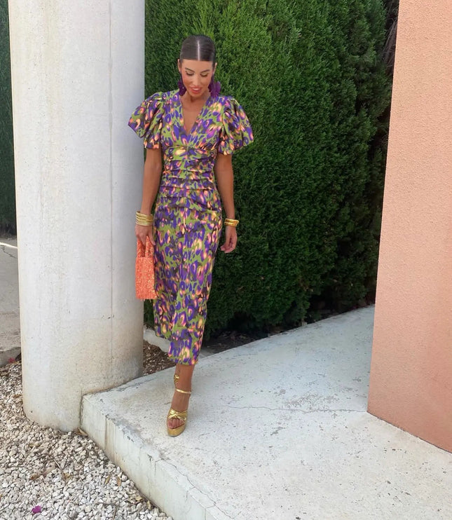 Full view of a women's cocktail dress in a green and purple floral pattern, featuring puff sleeves, V-neck, and midi length, paired with gold heels.
