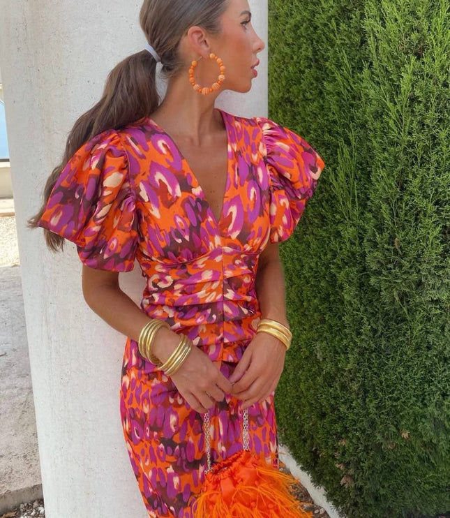 Women's cocktail dress in a vibrant orange and purple floral pattern with puff sleeves and a V-neck, cinched waist, and midi length.