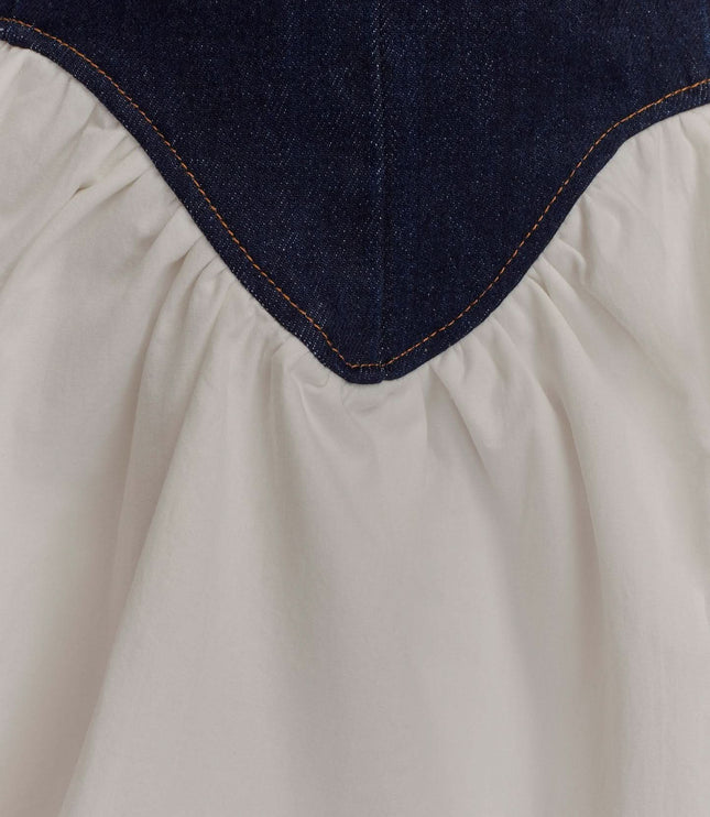 Detail close-up of pointed denim corset waist and gathered white skirt on mini dress