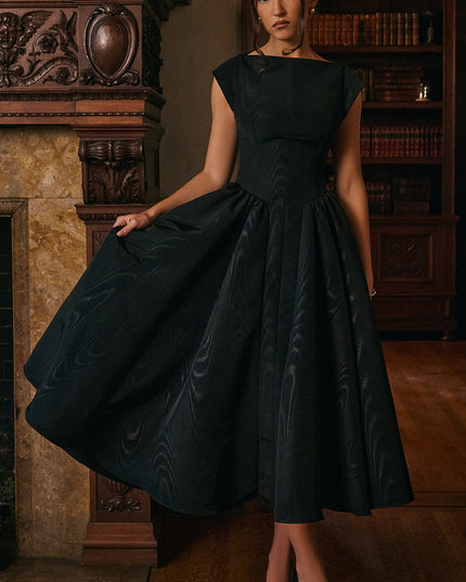Model wearing black open back midi cocktail dress in a library setting