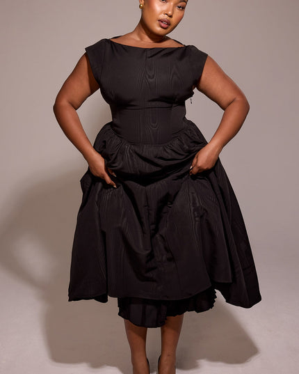 Black midi cocktail dress with open back, shown in front of ornate wood paneling