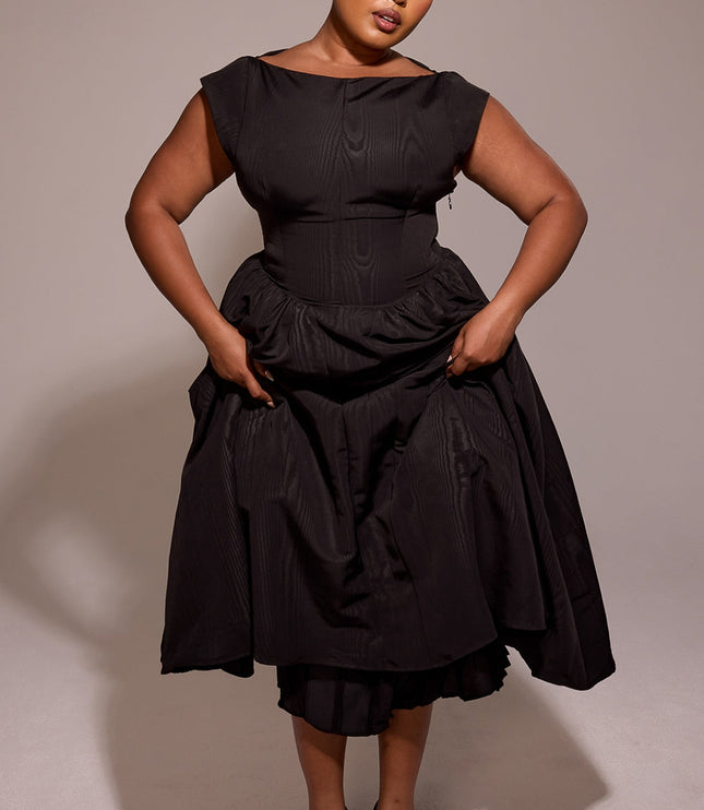 Black midi cocktail dress with open back, shown in front of ornate wood paneling
