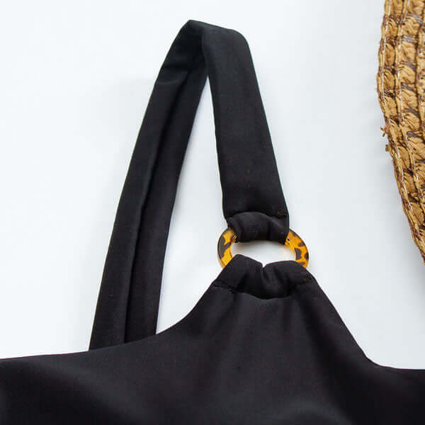 Close-up of black swimsuit strap and tortoiseshell ring detail on one piece swimsuit