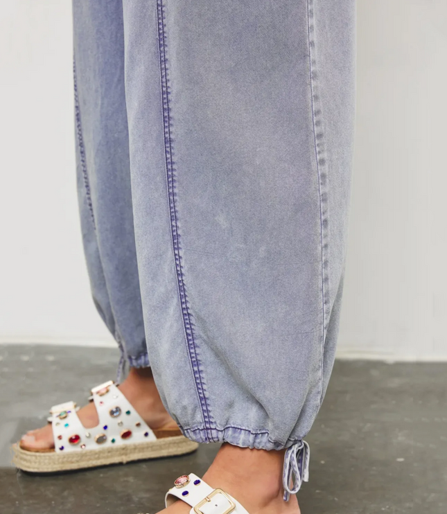 Close-up of light blue denim jumpsuit hem with drawstring detail and ankle cuff