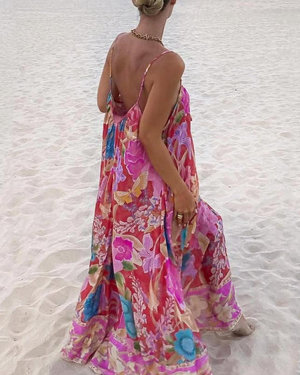 Back view of a women's floral print V-neck maxi sundress with thin straps, showcasing the colorful pattern on a beach.
