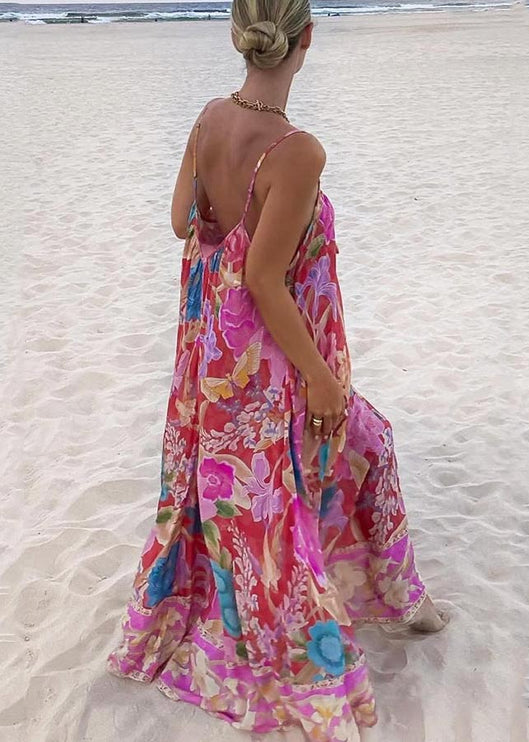 Back view of a women's floral print V-neck maxi sundress with thin straps, showcasing the colorful pattern on a beach.