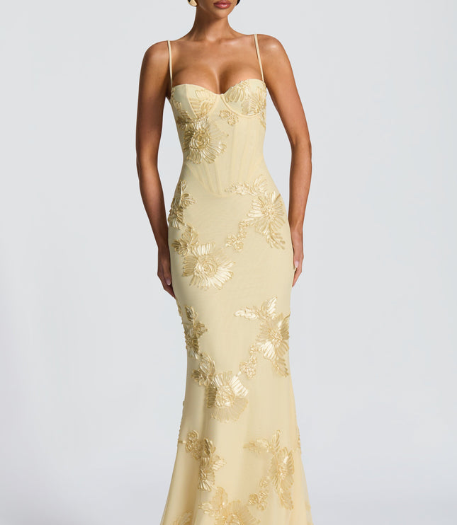 Front view of a women's formal light yellow maxi dress, showcasing detailed floral embroidery on the bodice and skirt, with a fitted silhouette.