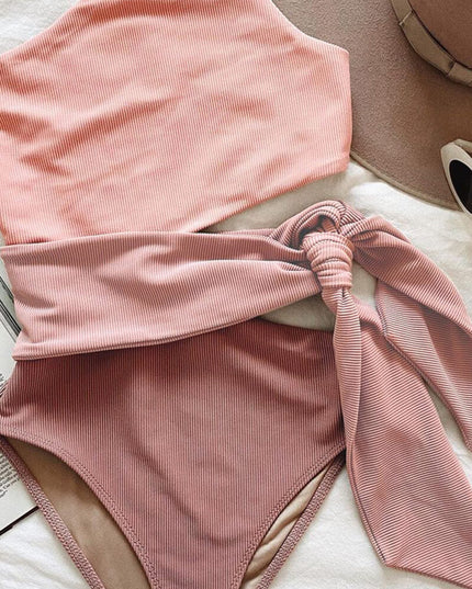 Folded pink ribbed one piece swimsuit with one shoulder cutout and matching waist tie
