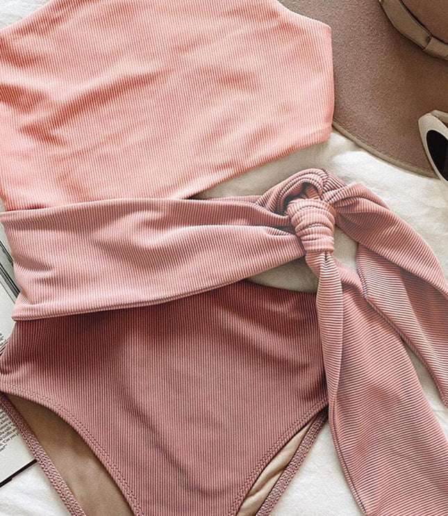 Folded pink ribbed one piece swimsuit with one shoulder cutout and matching waist tie