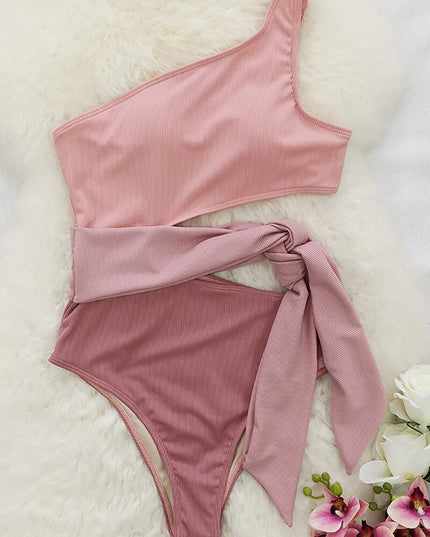Flat lay of pink one shoulder one piece swimsuit with cutout waist tie on white fur