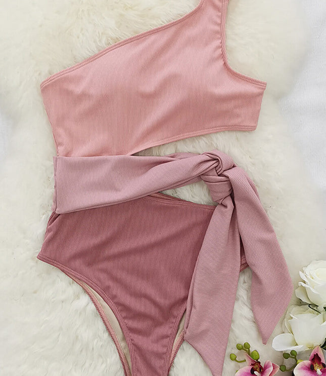 Flat lay of pink one shoulder one piece swimsuit with cutout waist tie on white fur