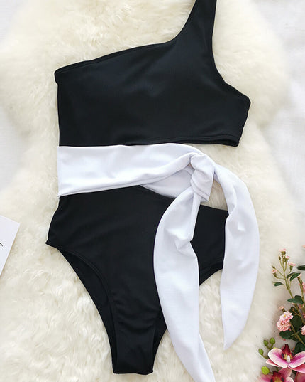 Flat lay of black one shoulder one piece swimsuit with white waist tie and cutout