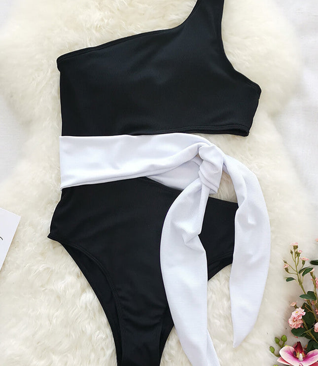 Flat lay of black one shoulder one piece swimsuit with white waist tie and cutout