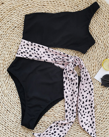 Black one shoulder one piece swimsuit with pink leopard print waist tie in flat lay