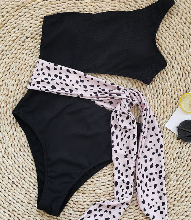Black one shoulder one piece swimsuit with pink leopard print waist tie in flat lay