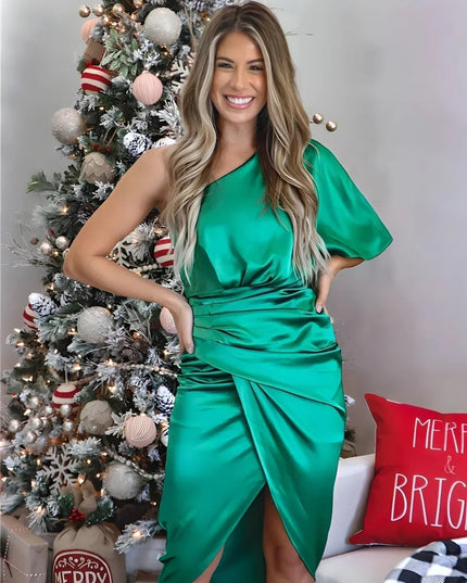 Smiling woman in a vibrant green one shoulder draped satin midi dress with a festive Christmas tree background
