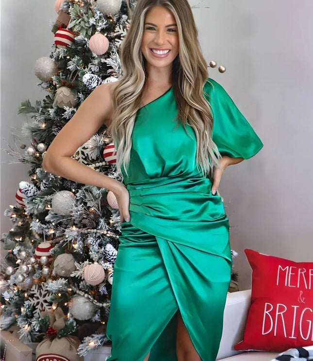 Smiling woman in a vibrant green one shoulder draped satin midi dress with a festive Christmas tree background
