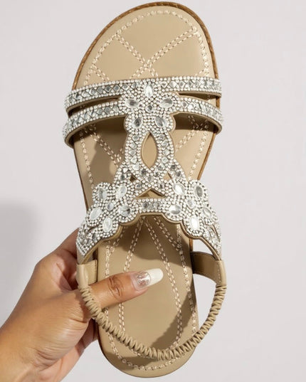 Beige embellished flat sandal held in hand showing crystal detail